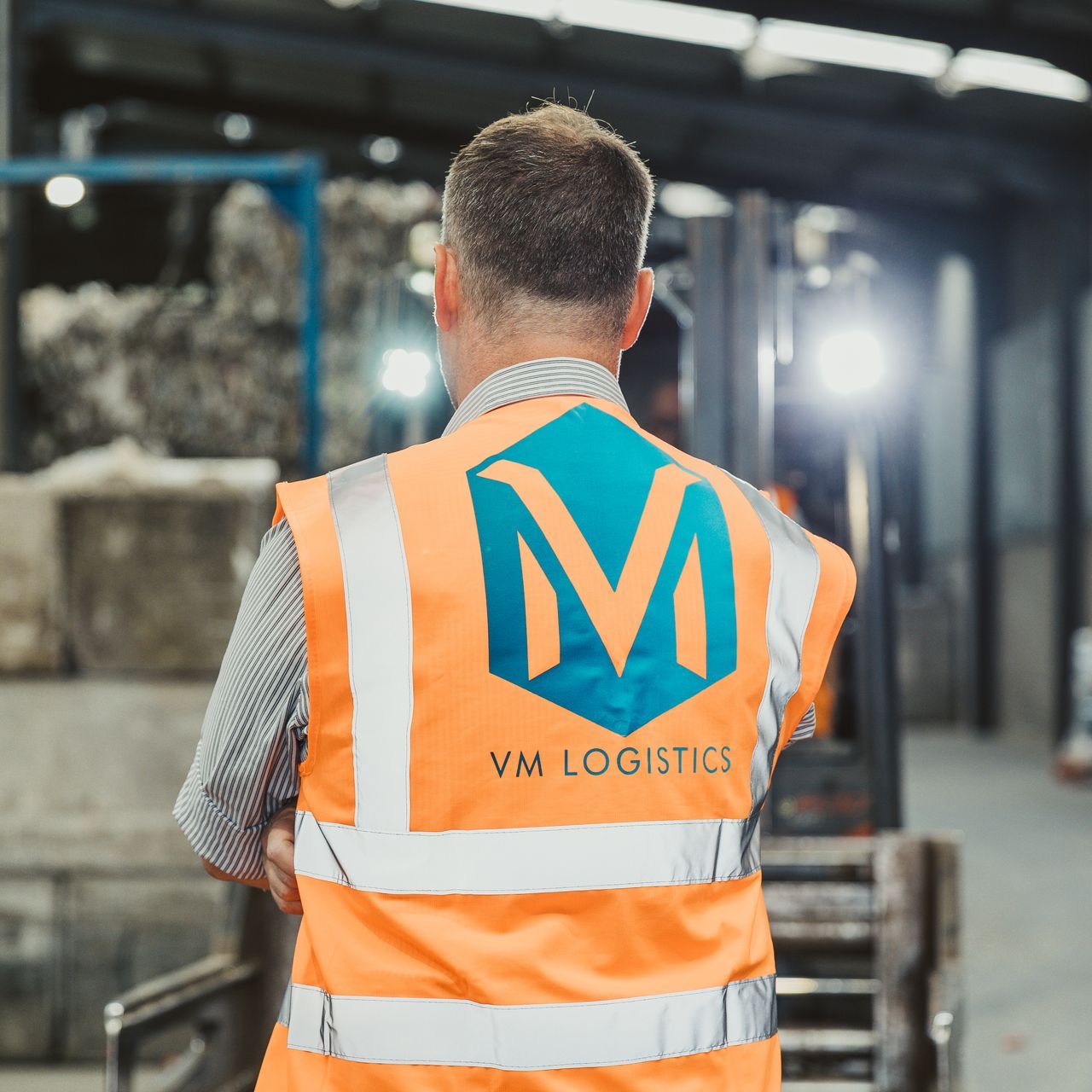 Een man met een oranje vest met de tekst vm logistics
