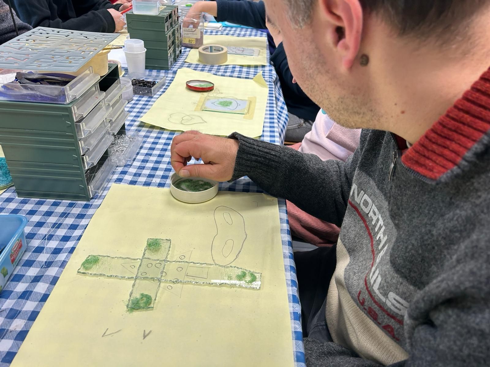 Un uomo è seduto a un tavolo e usa un righello per disegnare una croce su un pezzo di carta.