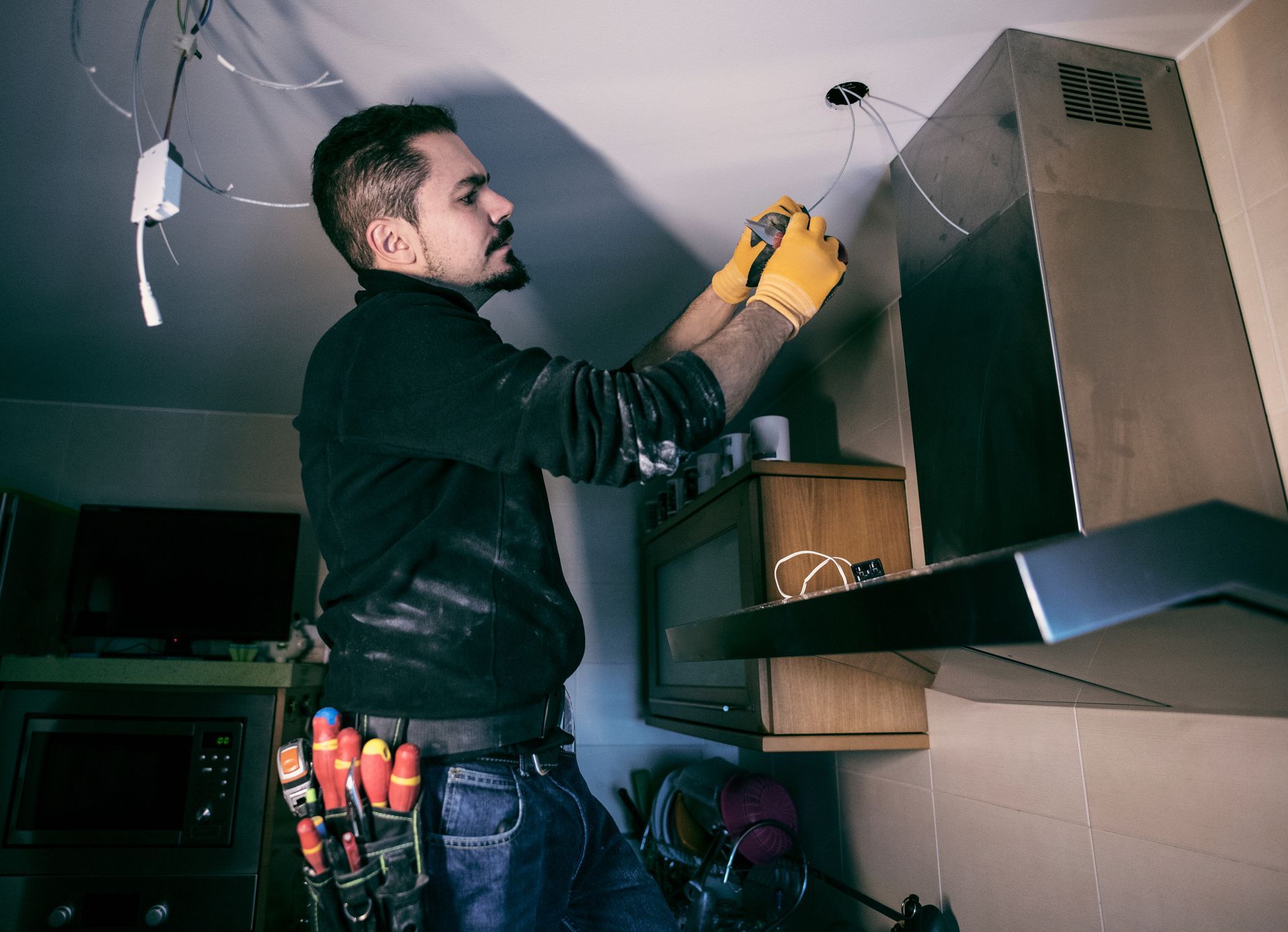A man wearing a black shirt and gloves installs the electrical circuit of a kitchen appliance.