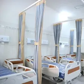 Hospital room with several empty white beds and blue privacy curtains