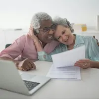 Two people smiling at a desk, reading a document beside a laptop