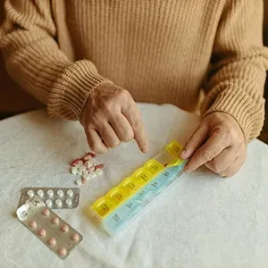 Person sorting pills into a yellow-blue pill organizer on a white table.