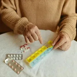 Person sorting pills into a yellow-blue pill organizer on a white table.
