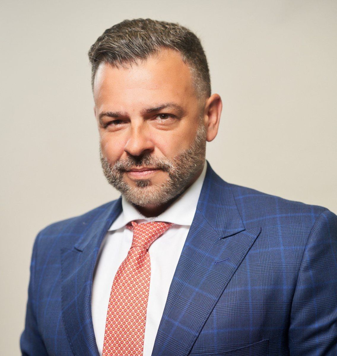 A man with a beard wearing a blue suit and red tie