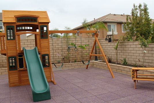 A wooden playground with a slide and swings in a backyard.