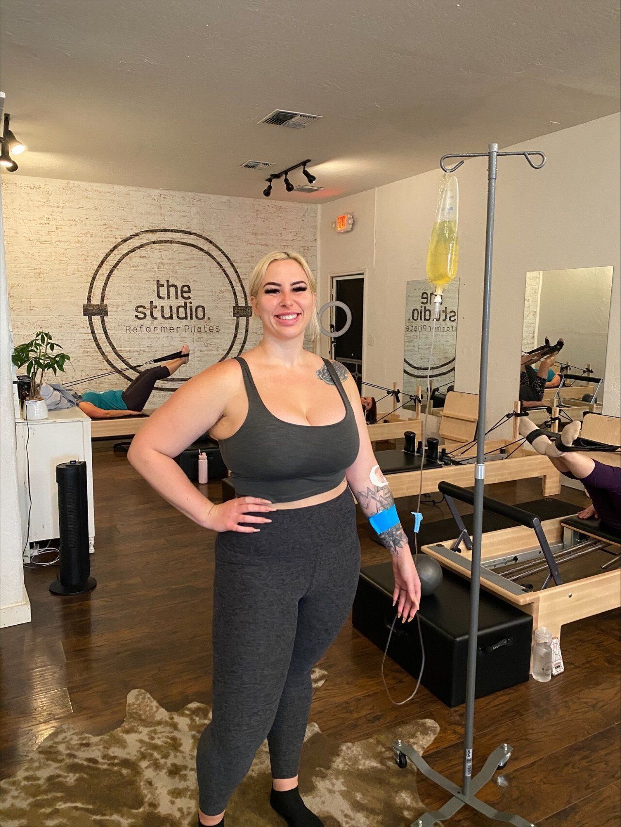 women smiling beside an IV drip stand in a fitness studio.