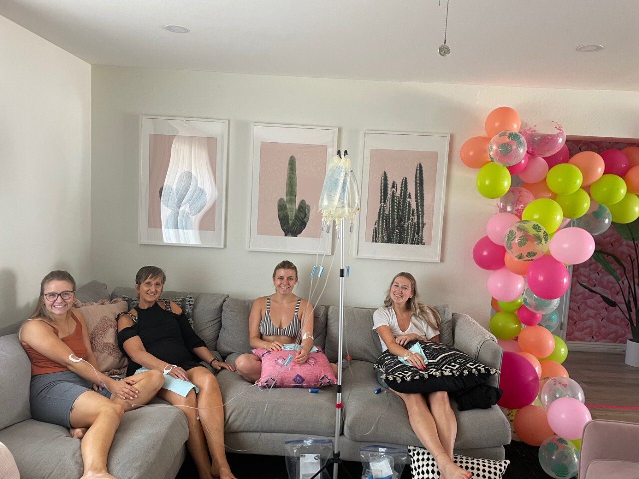 Four people receiving IV therapy on a couch with IV bags in a decorated room.