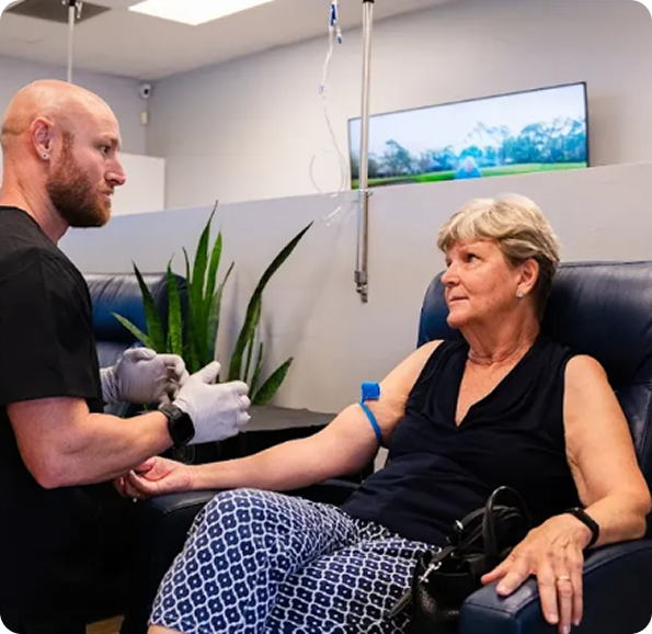 Medical professional preparing an IV drip for a seated patient in a clinic.