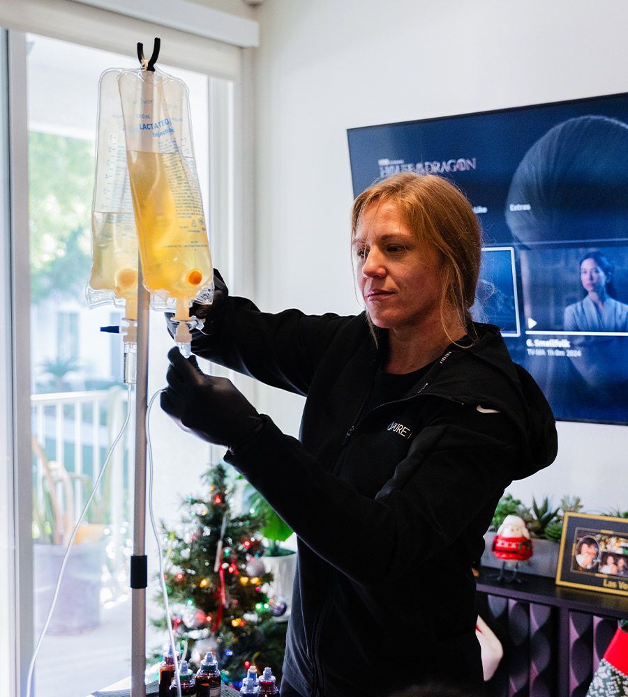 Woman preparing IV drip bag in a home setting; Christmas tree and TV in the background.
