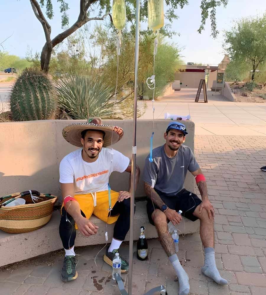 Two men outdoors by a cactus receiving post-activity IV hydration for recovery