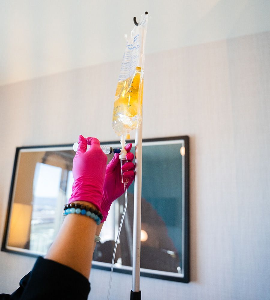 Hands in pink gloves adjusting an IV bag filled with yellow liquid, hanging from a metal stand.