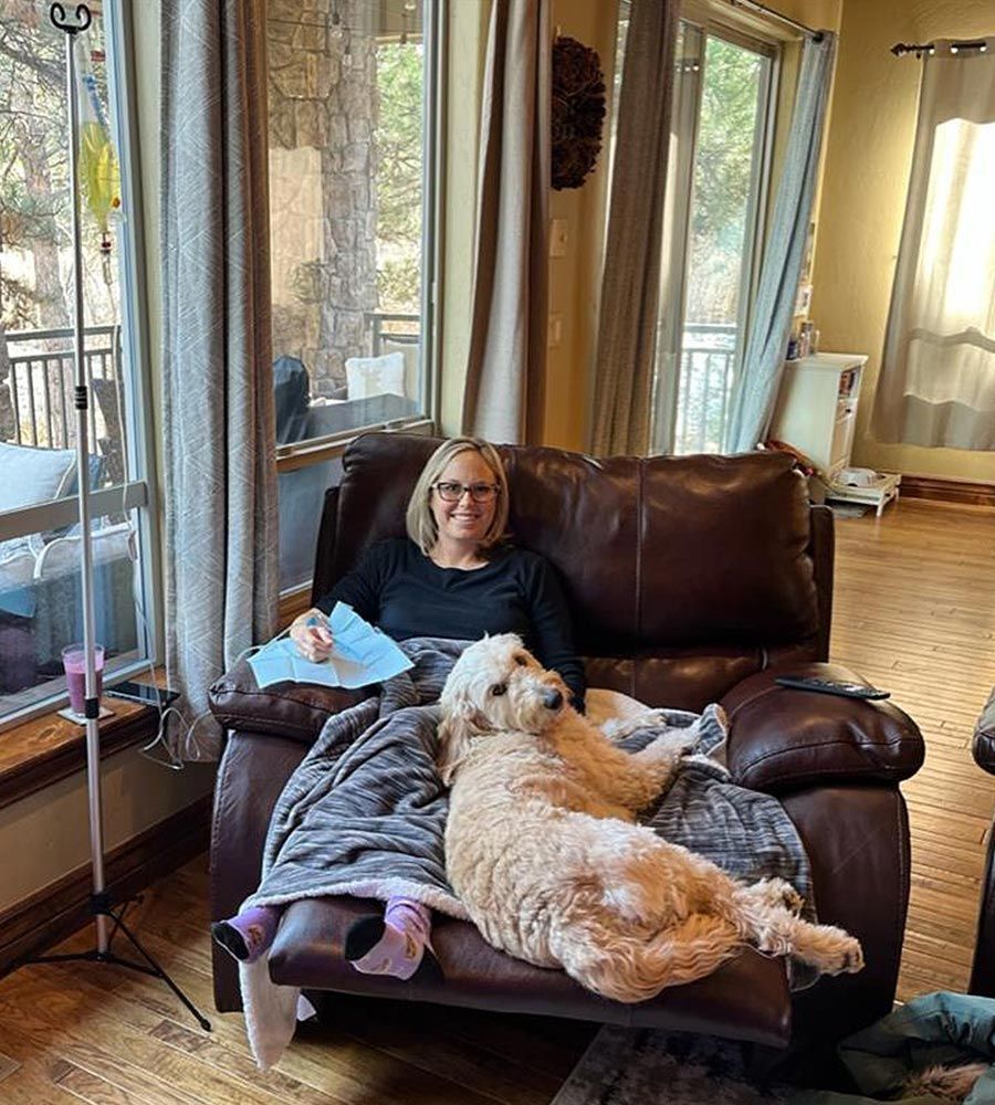Woman in recliner with dog, receiving IV infusion near window.