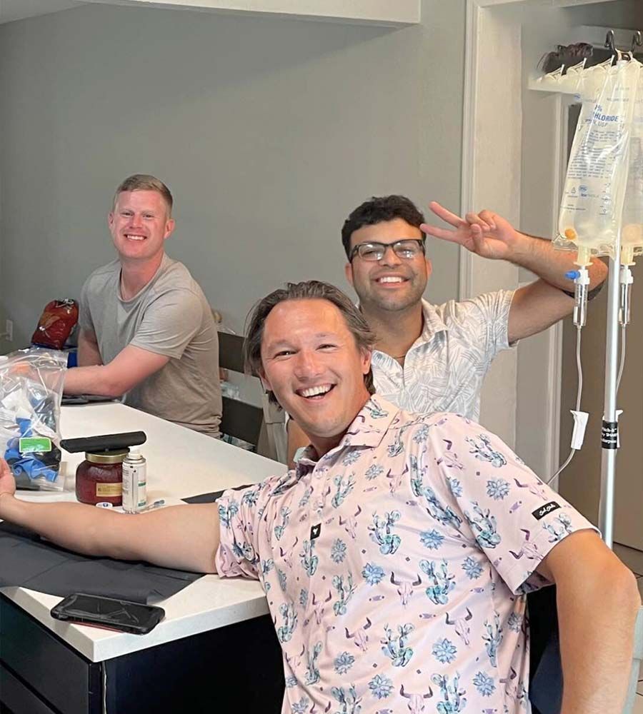 Three men receiving group IV hydration therapy with IV bags visible.