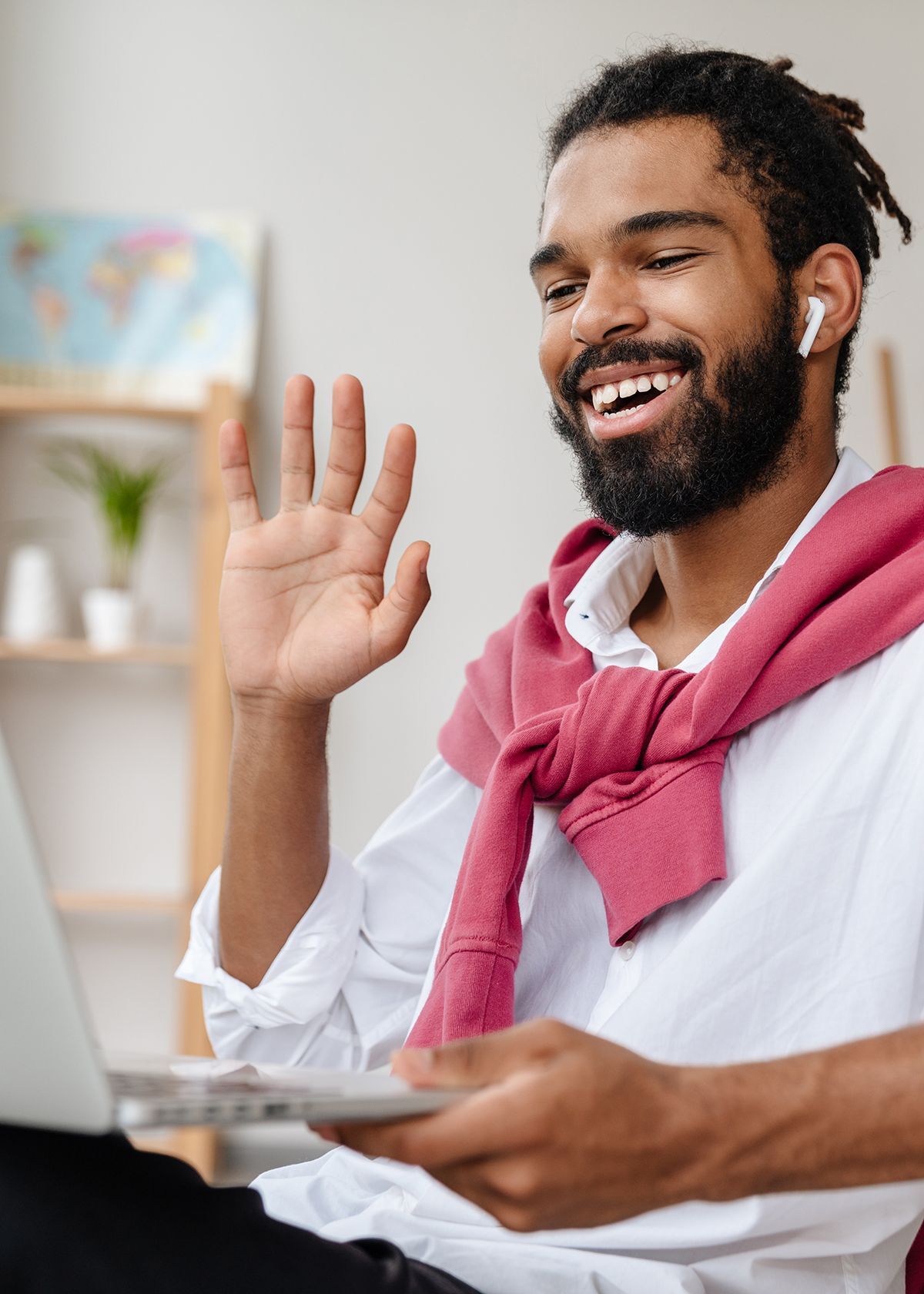 Person smiling and waving during a video call wearing a white shirt and pink sweater