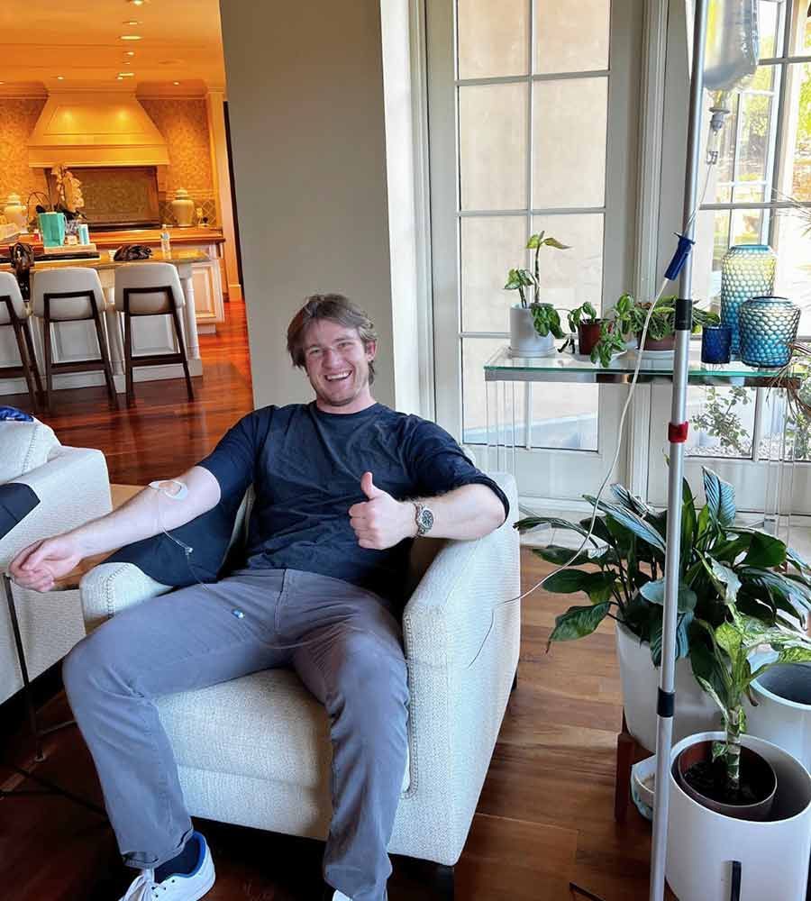 Happy man receiving mobile IV therapy at home while giving a thumbs up.