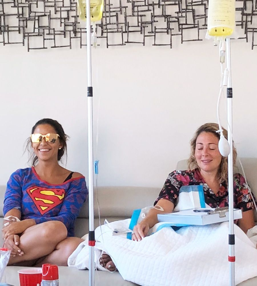 Two patients receiving IV therapy on a sofa, smiling and relaxing.