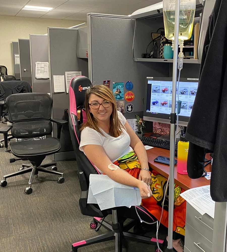 Woman seated at a desk, receiving an IV drip in an office setting.