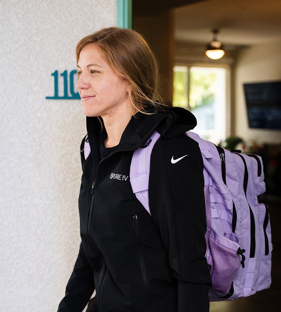 A person in a black Nike jacket and a light purple backpack walking past a wall with the number 110.