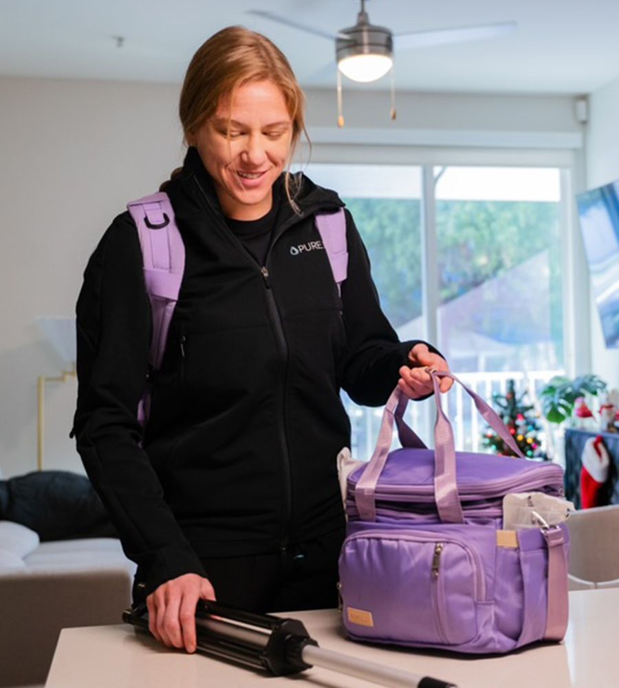 Person in a black jacket and purple backpack setting a tripod beside a purple gear bag.