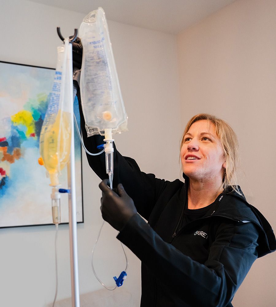 Person in black clothing and gloves adjusting IV bags on a pole near an abstract painting