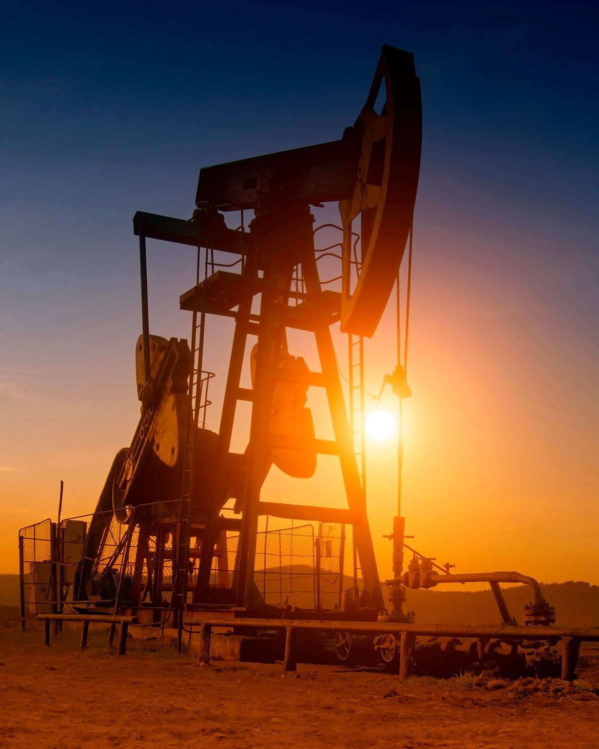 A silhouette of an oil pump jack against a bright, orange sunset.