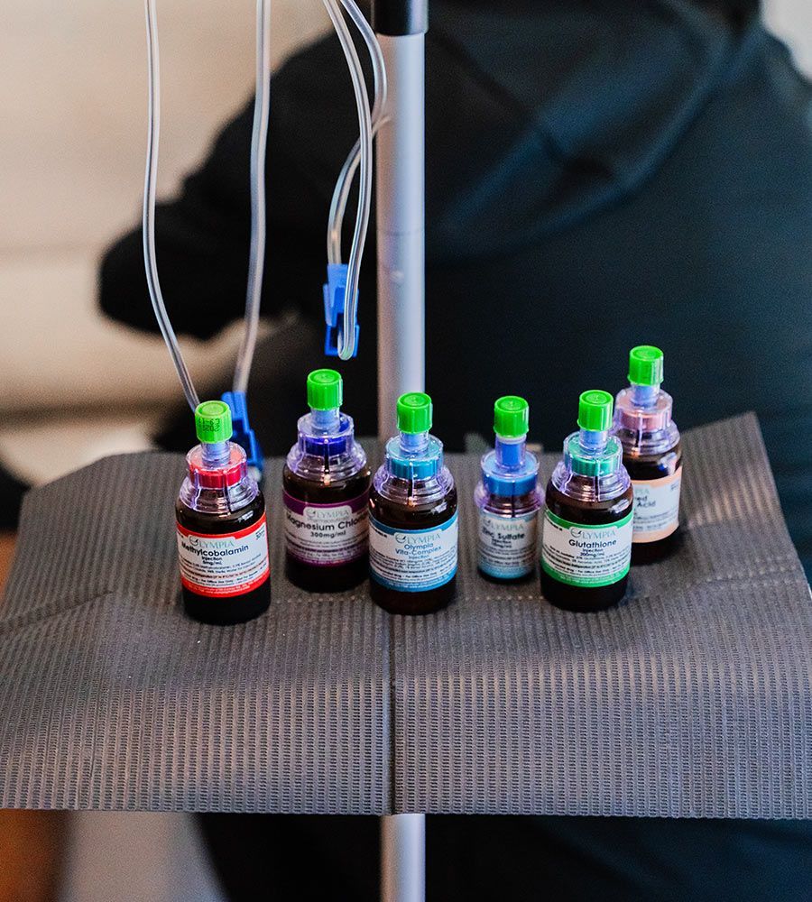Bottles of tattoo ink with green lids on a tray, tubes above. Person in black is blurred in the background.