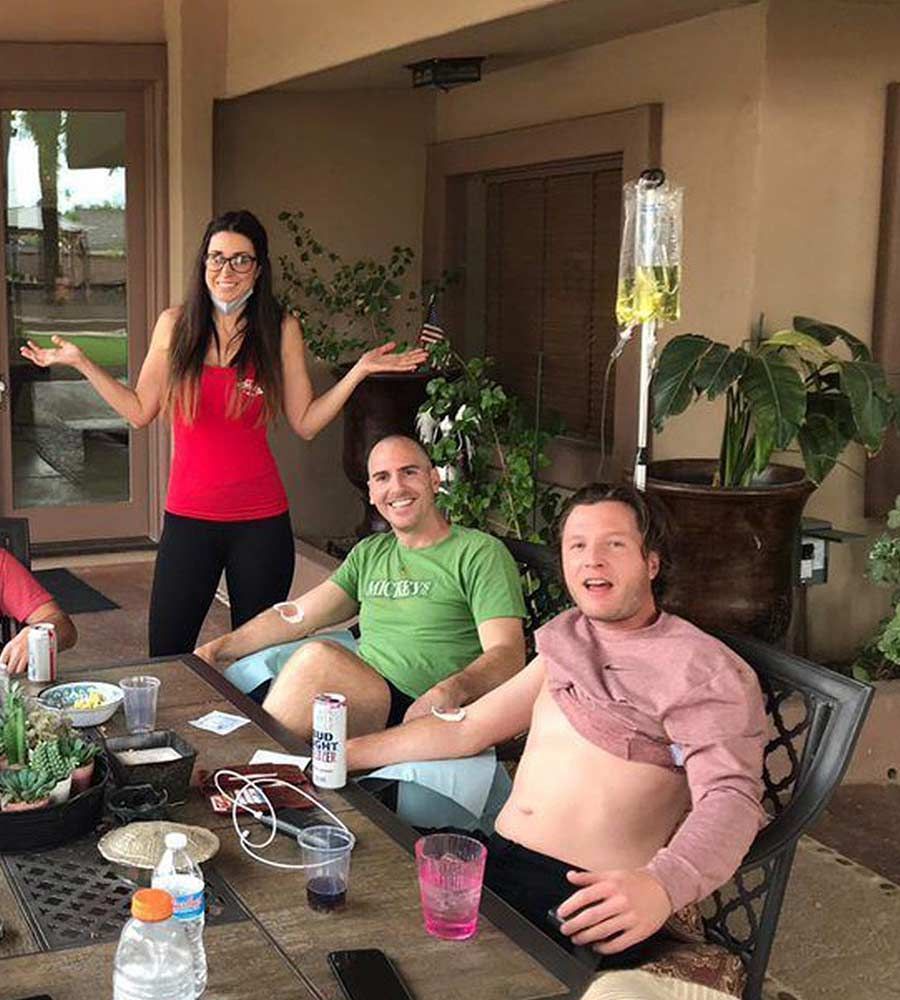 Three people receiving IV infusions on a patio. One woman and two men, all smiling, relaxed, with IV bags visible.