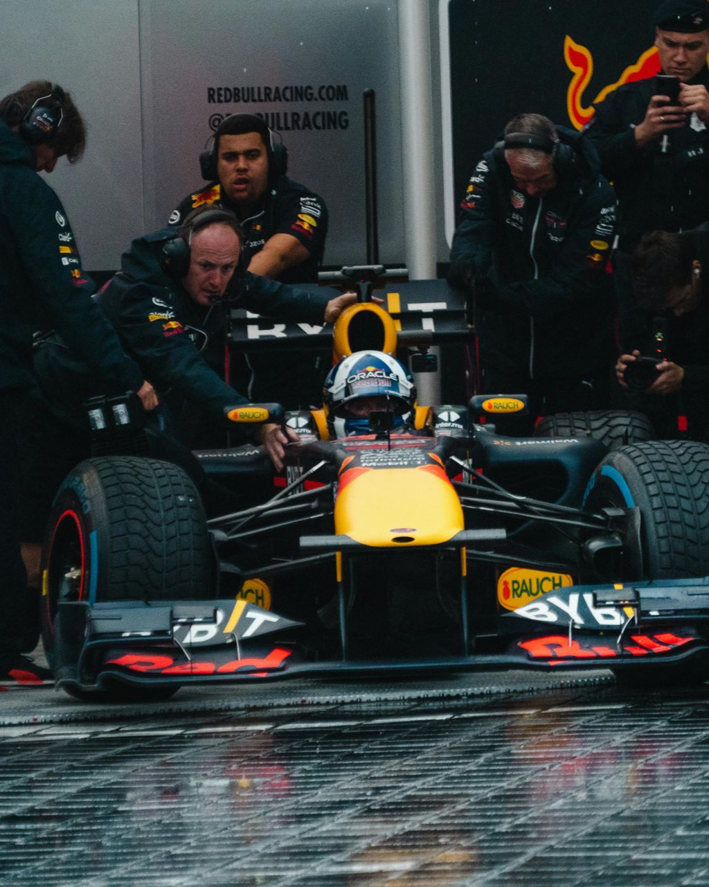 Formula 1 race car in a wet pit lane with crew members around it during a rain-soaked race stop