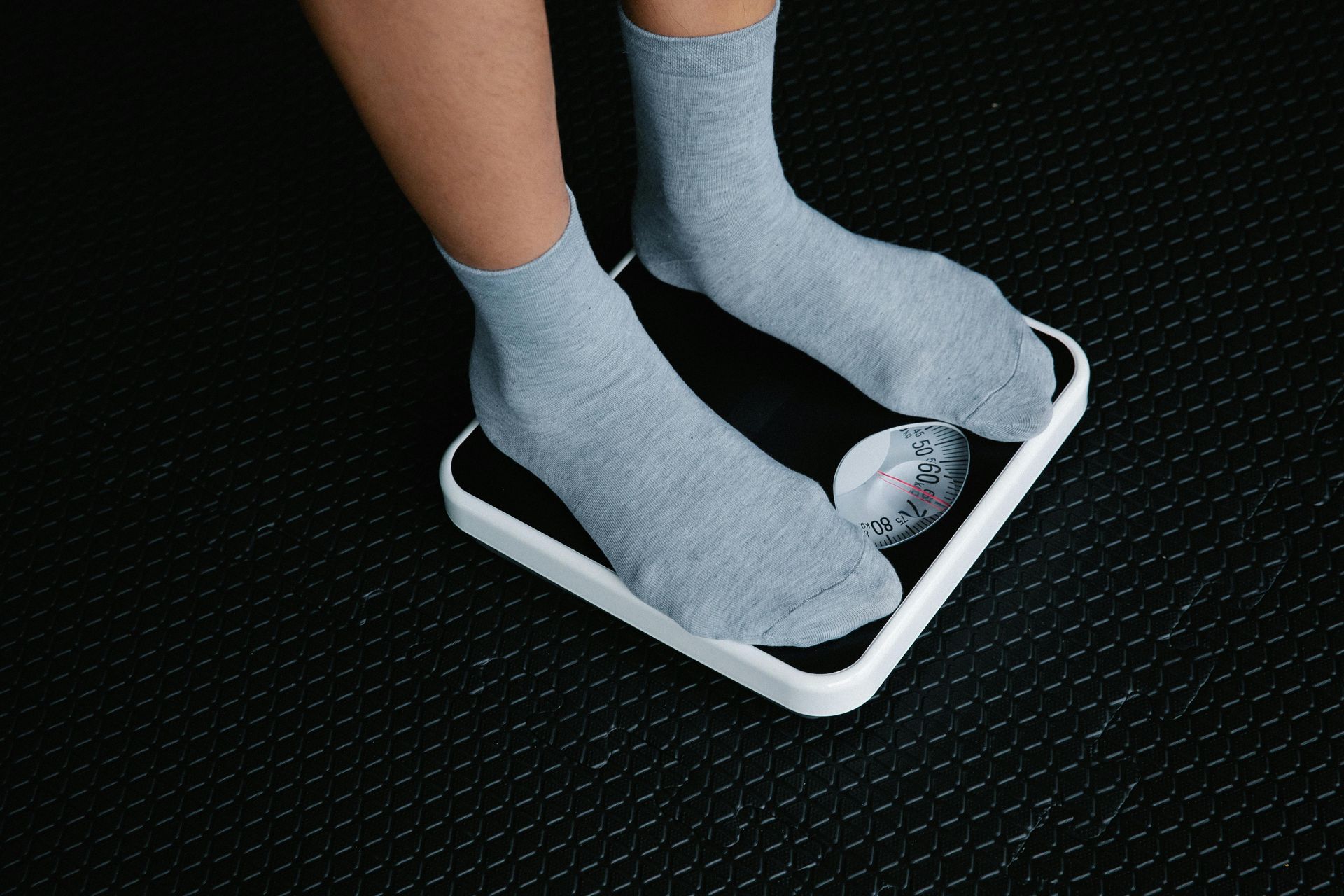 Feet in gray socks standing on a black and white scale on a black floor.