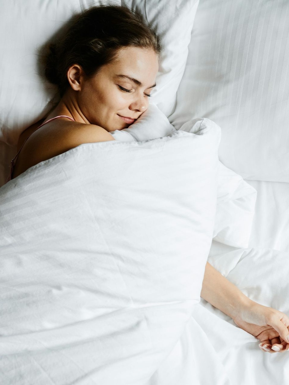 A person sleeping peacefully in a bed with white linens and pillows, resting their head on a soft, white pillow.