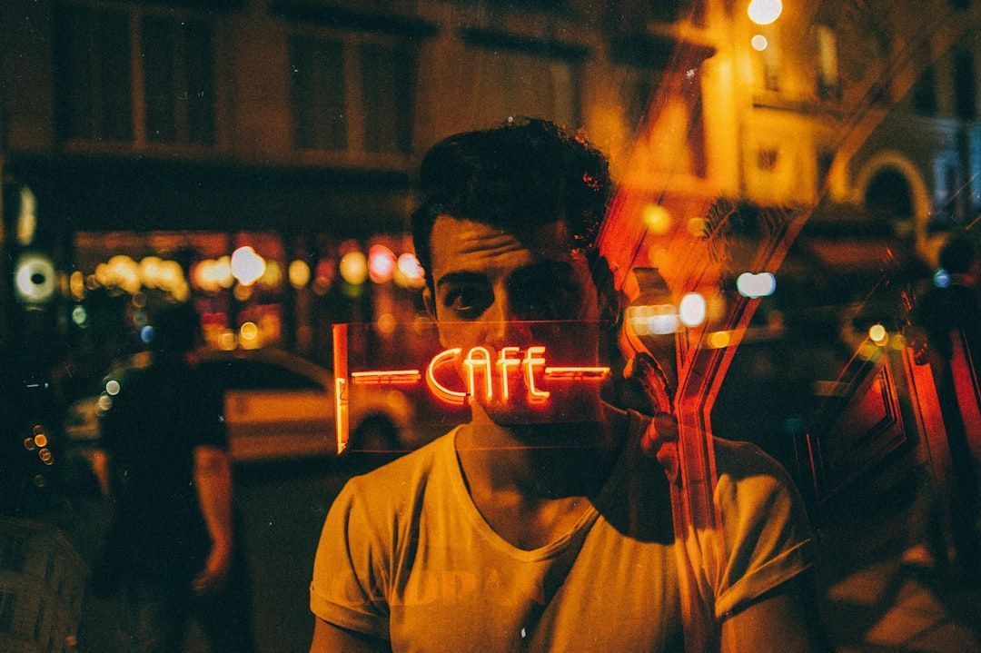 A person in a yellow t-shirt stands behind a window with a glowing orange neon 