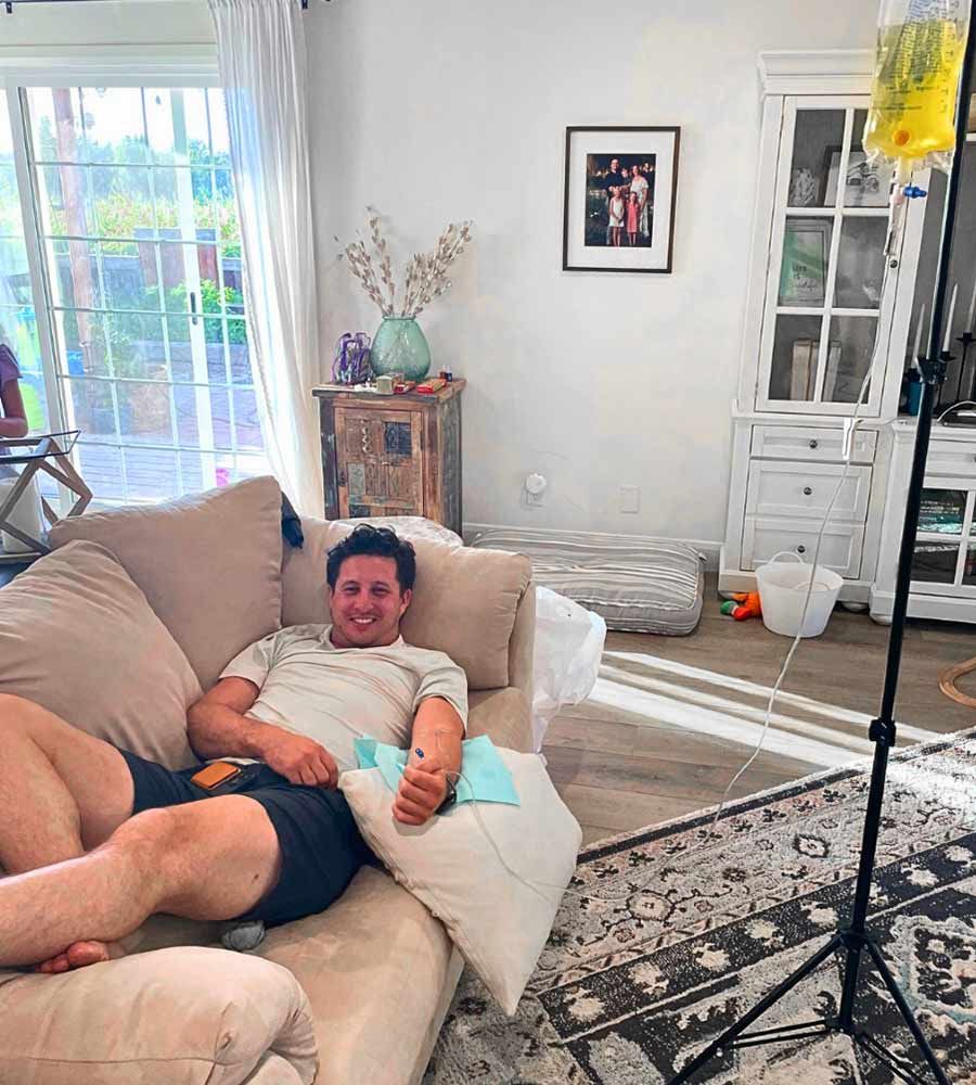 Man reclining on a couch receiving at-home IV therapy for nausea with a smile