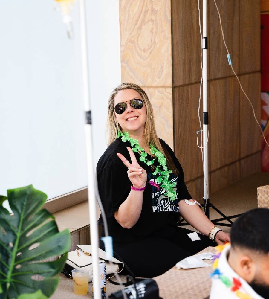 Smiling female client receiving mobile IV therapy for hangover recovery at a pool party.