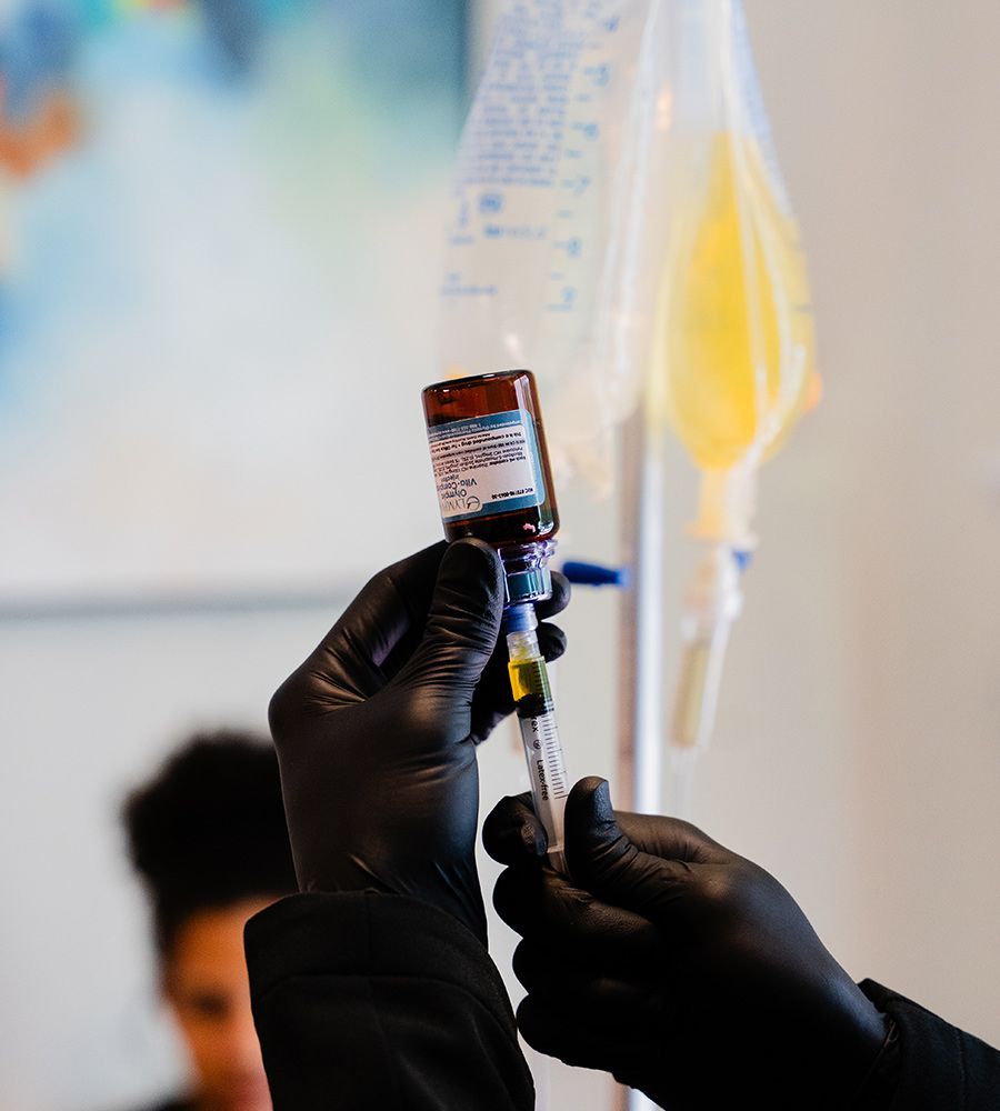 Hands in black gloves preparing an altitude sickness IV bag, syringe withdrawing liquid.