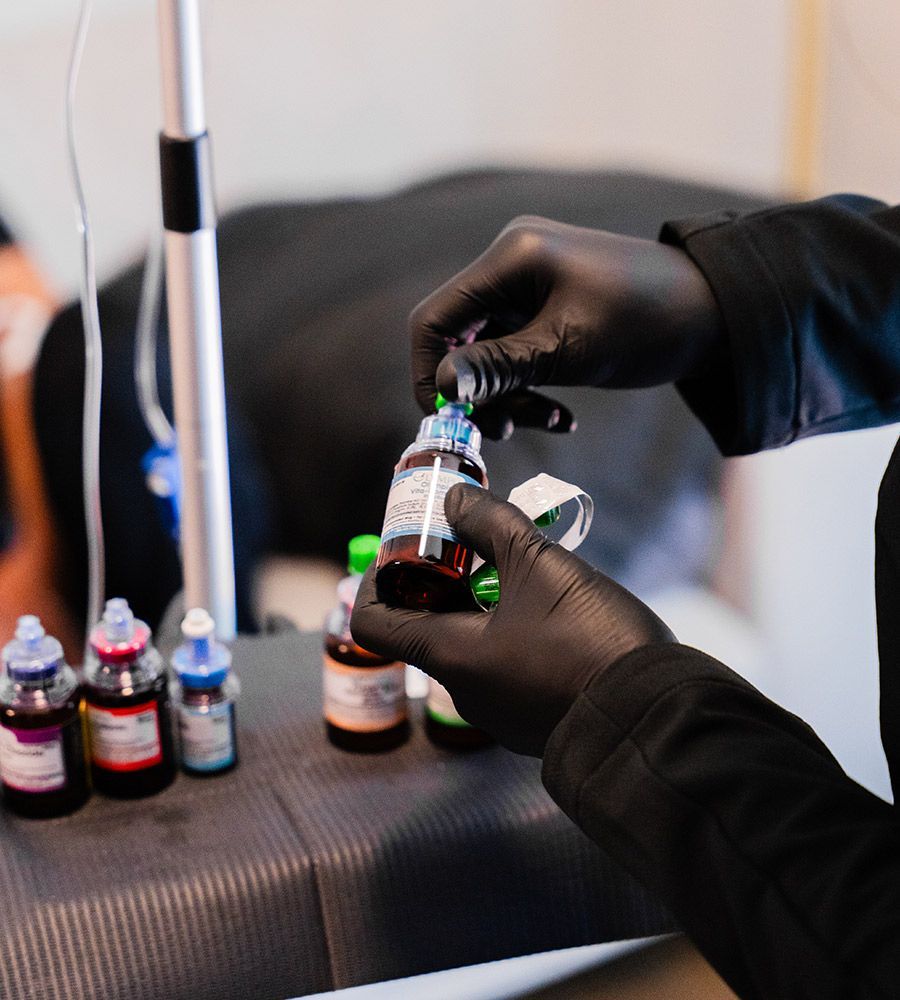 Person wearing black gloves preparing tattoo ink bottles, with other colors visible.