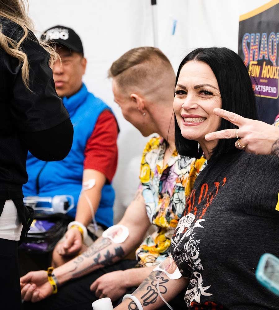 People with IVs smile. A woman gives a peace sign. A person wears a colorful shirt.