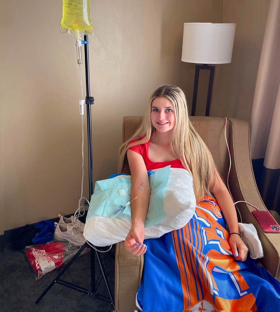 Young woman with long blonde hair receiving an IV infusion while relaxing in an armchair.