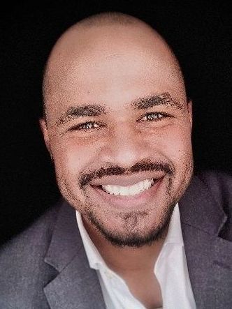 A bald man with a beard is smiling for the camera while wearing a suit and white shirt.