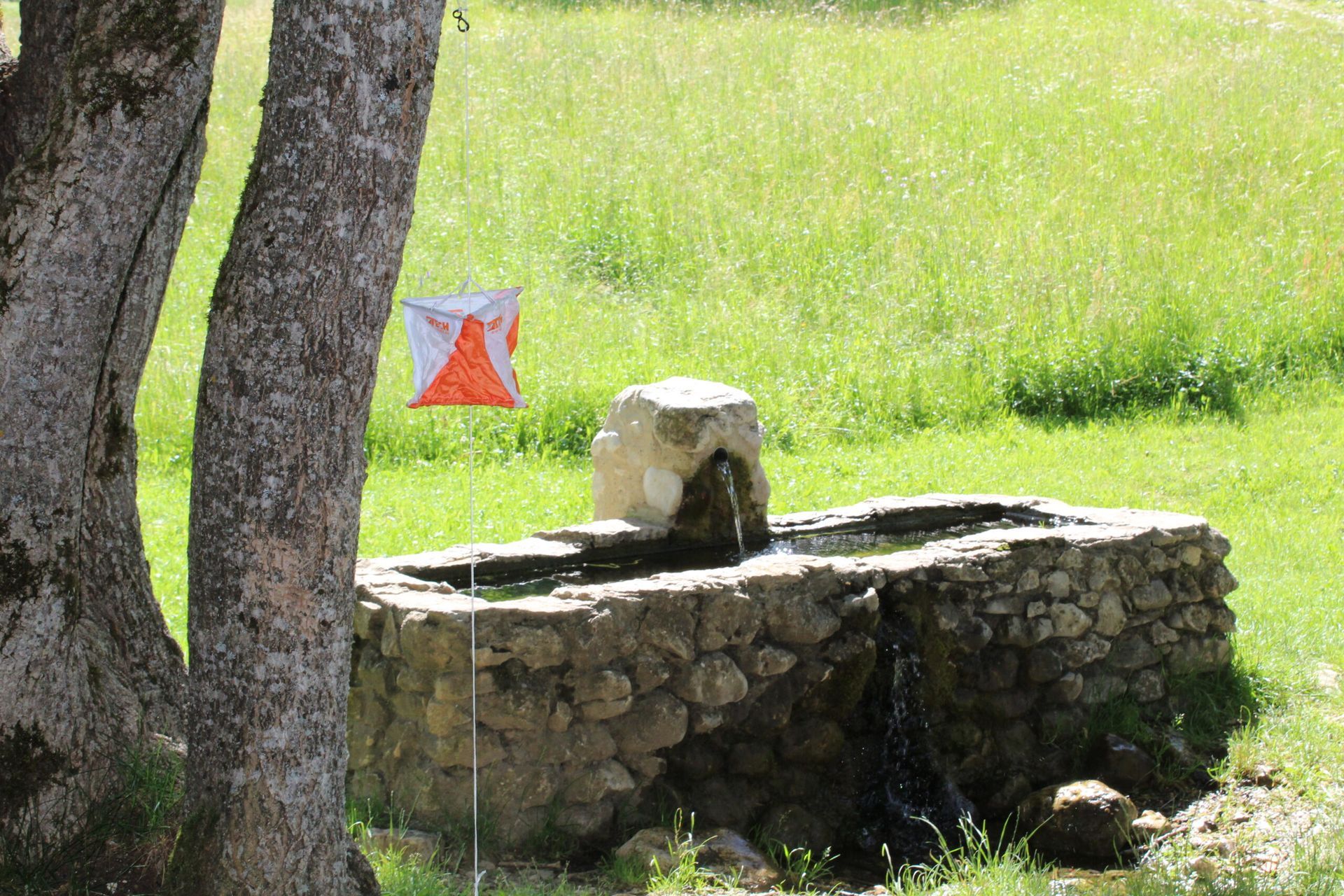 Une fontaine en pierre au milieu d'un champ herbeux avec un drapeau en arrière-plan.