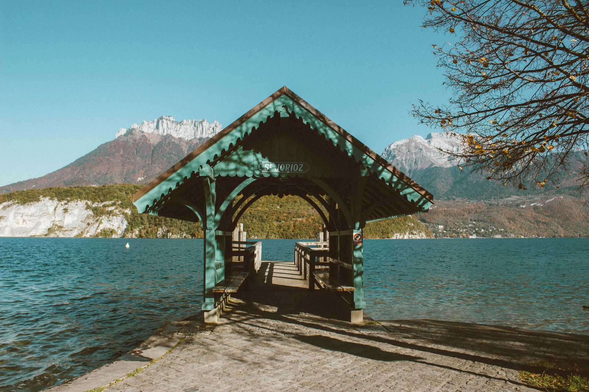 Une petite cabane est assise sur la rive d'un lac avec des montagnes en arrière-plan.