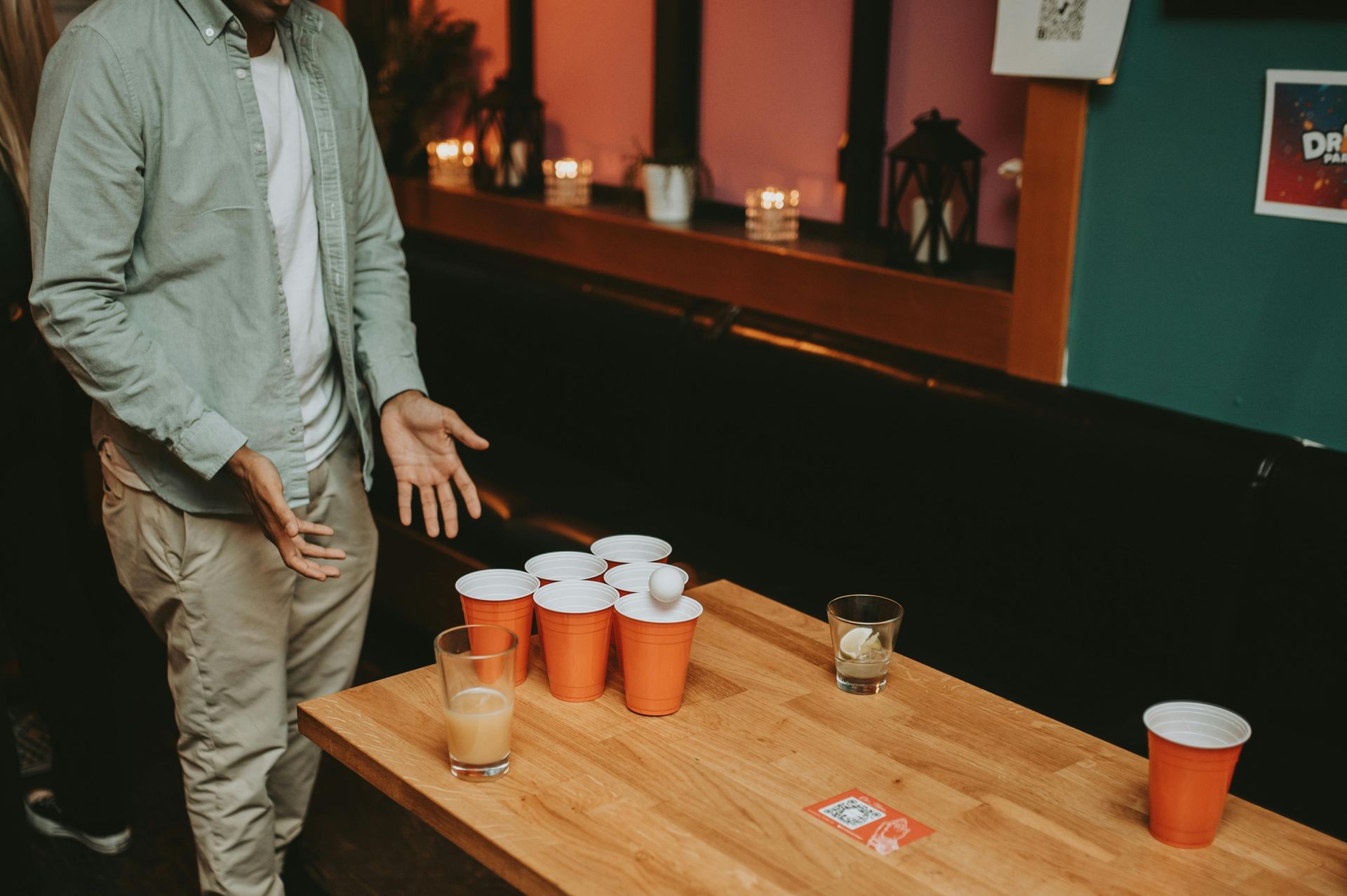 Un homme se tient debout à côté d'une table avec des tasses et des verres de bière-pong dessus.