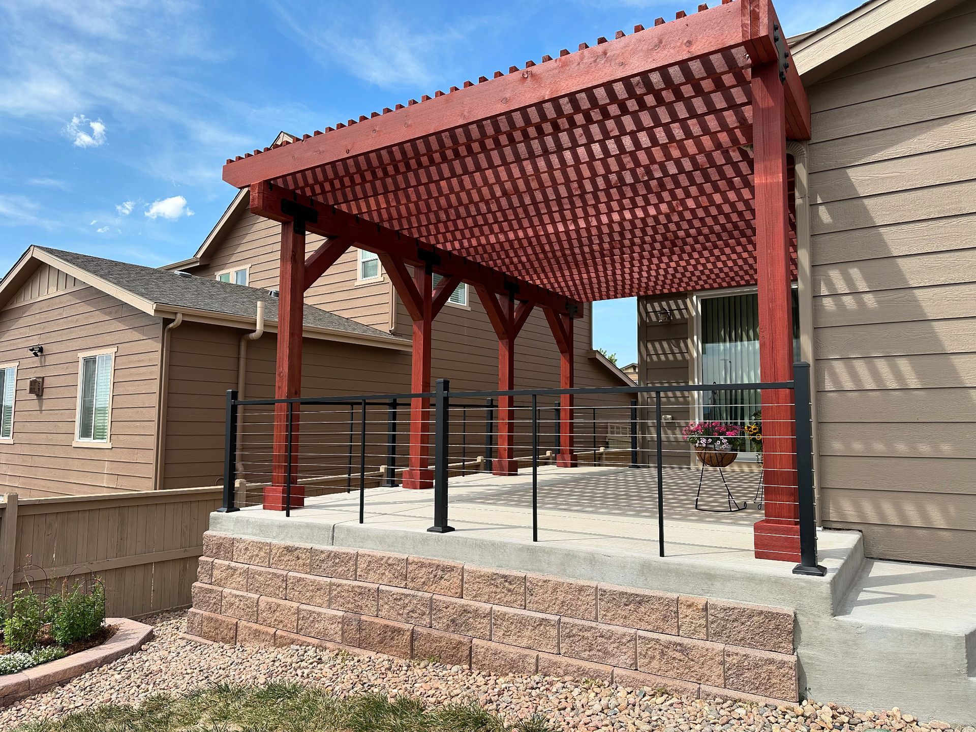 Covered backyard patio with red pergola roof, black railing, and concrete steps beside a house.