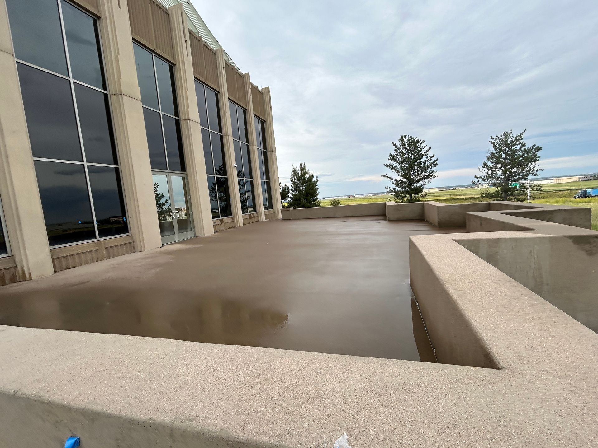 Modern building terrace with beige concrete walls, large windows, and cloudy sky over a distant landscape