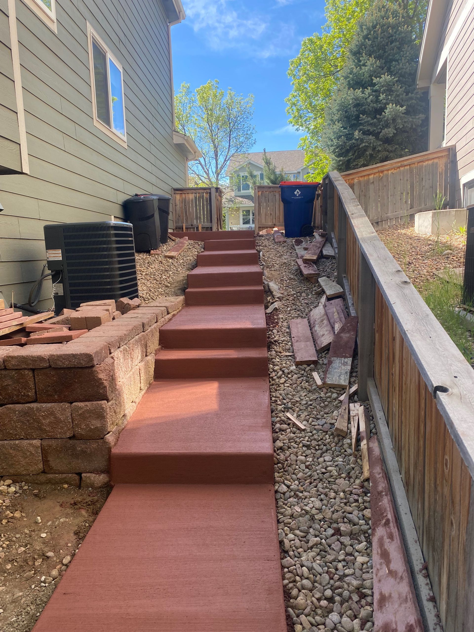 Steep outdoor walkway with red steps between houses, lined with rocks and retaining walls.