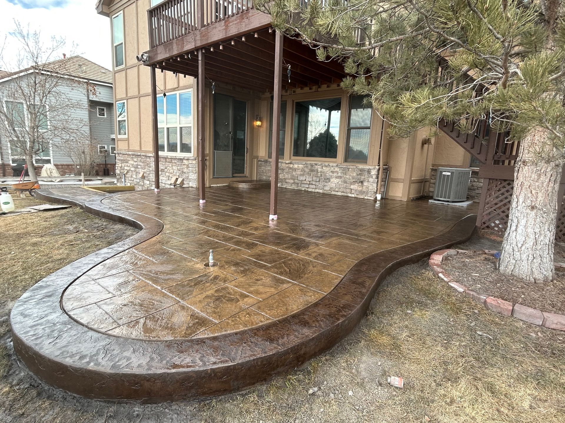 Wet stone patio curving around a house with a wooden deck and leafless trees in a yard