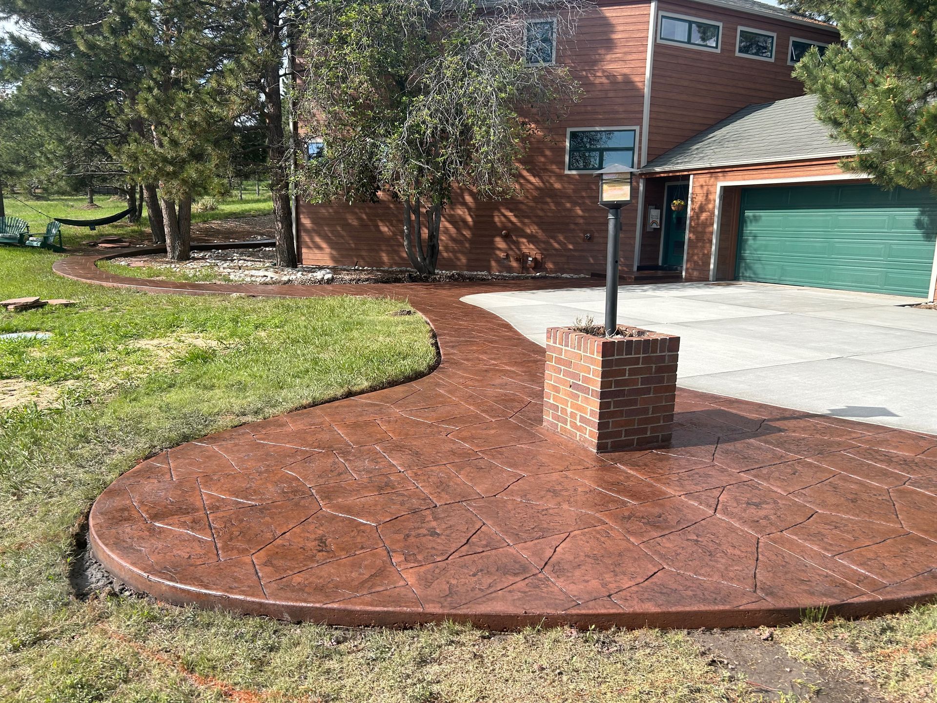 Curved red brick walkway leads to a driveway and green garage door beside a brick house and lawn.
