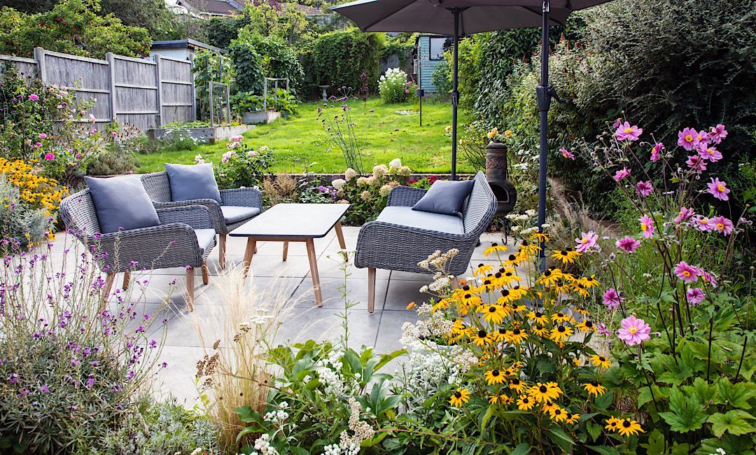 Backyard patio with gray chairs, coffee table, and colorful flowers in a sunny garden