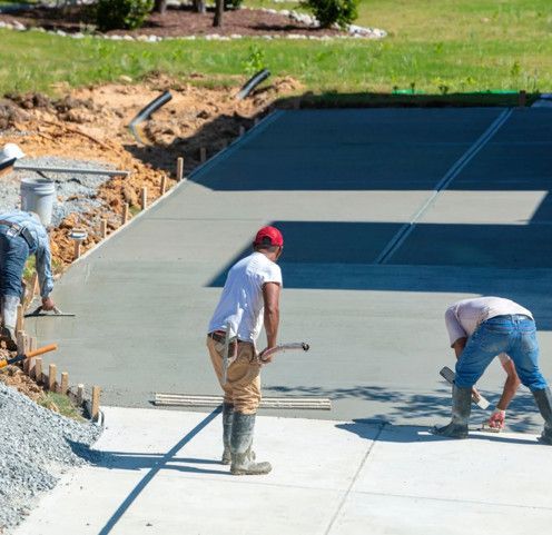 Workers smoothing wet concrete on a sloped driveway under construction