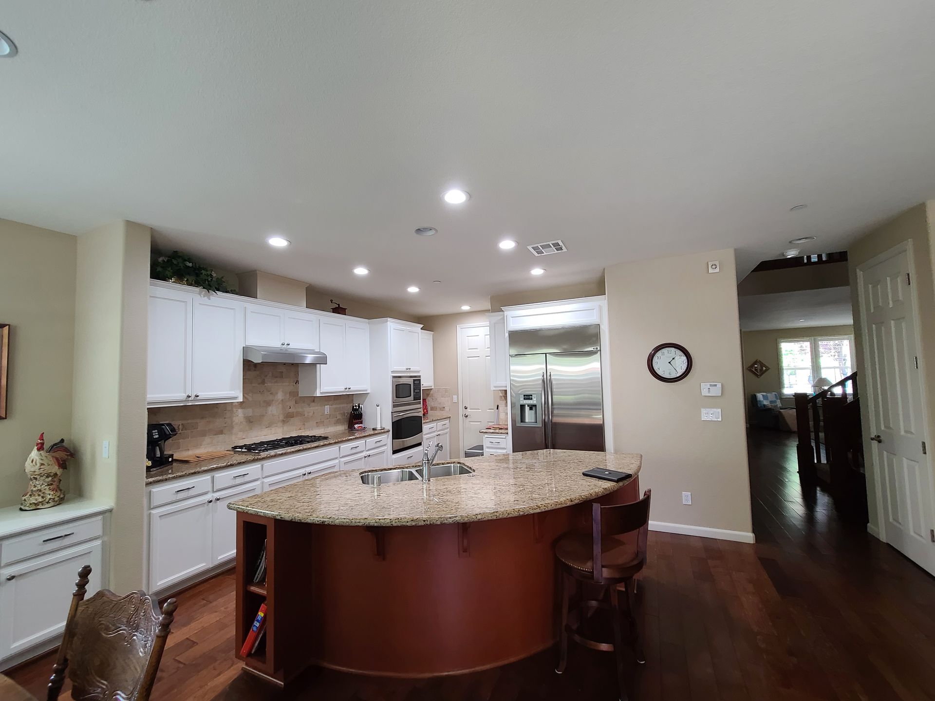 Spacious modern kitchen with granite island, white cabinets, stainless appliances, and dark wood floors