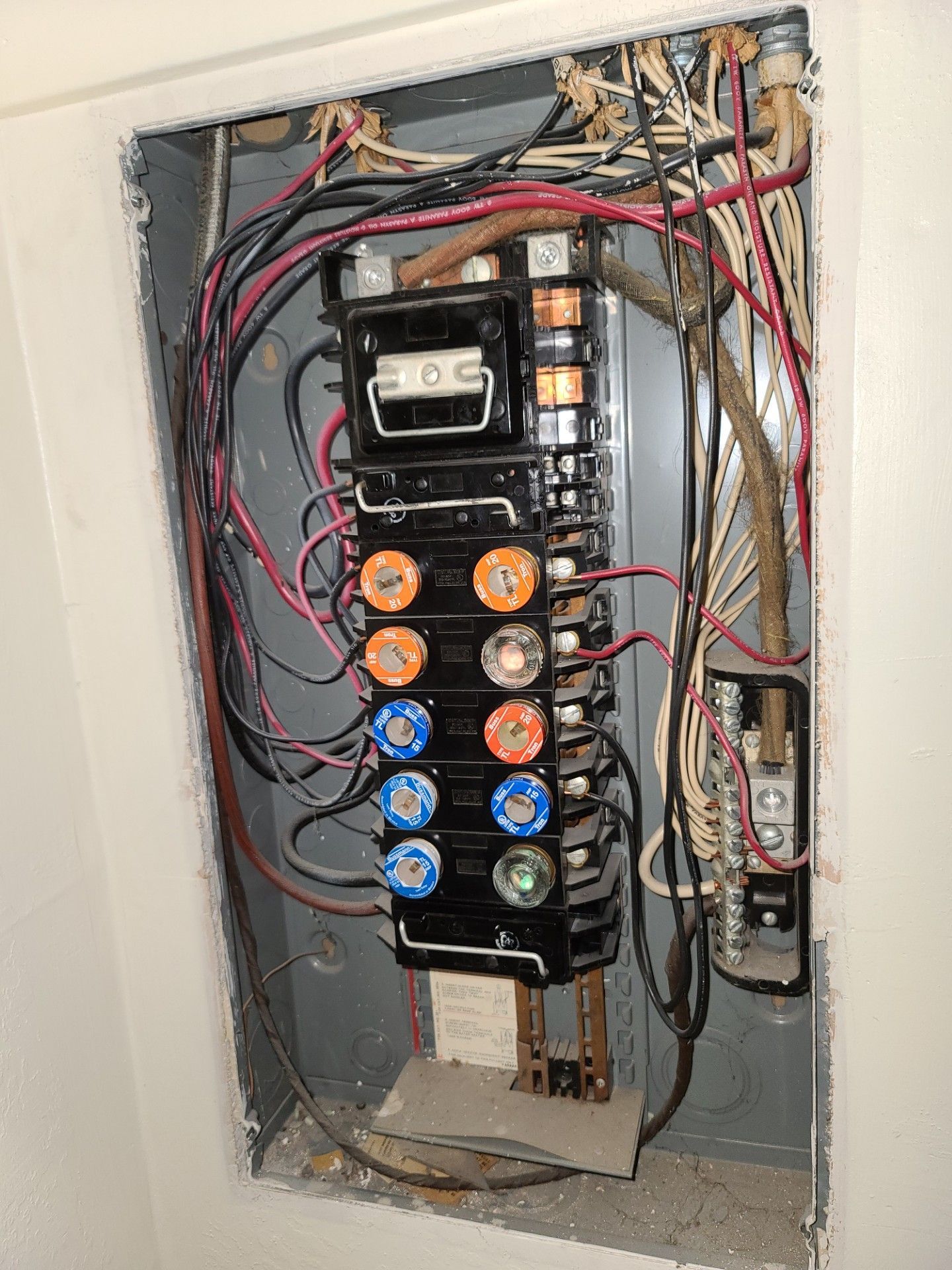 Open electrical breaker panel with exposed wires and colored circuit breakers mounted in a wall recess